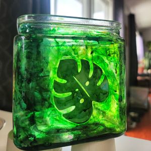 Glass jar with green liquid featuring a decorative monstera leaf design.