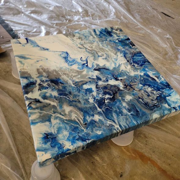 Abstract fluid art painting in shades of blue and white creating a marbled effect.