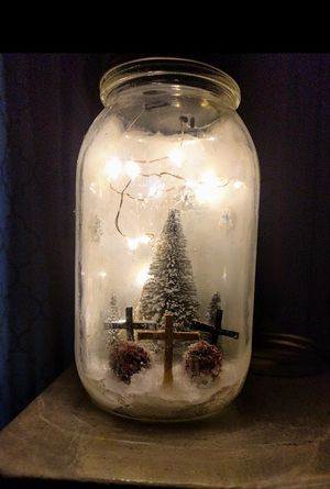 Illuminated mason jar snow globe with miniature Christmas tree and fence creating a magical winter scene.