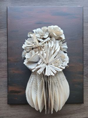 Paper sculpture of flowers crafted from book pages mounted on dark wooden background.