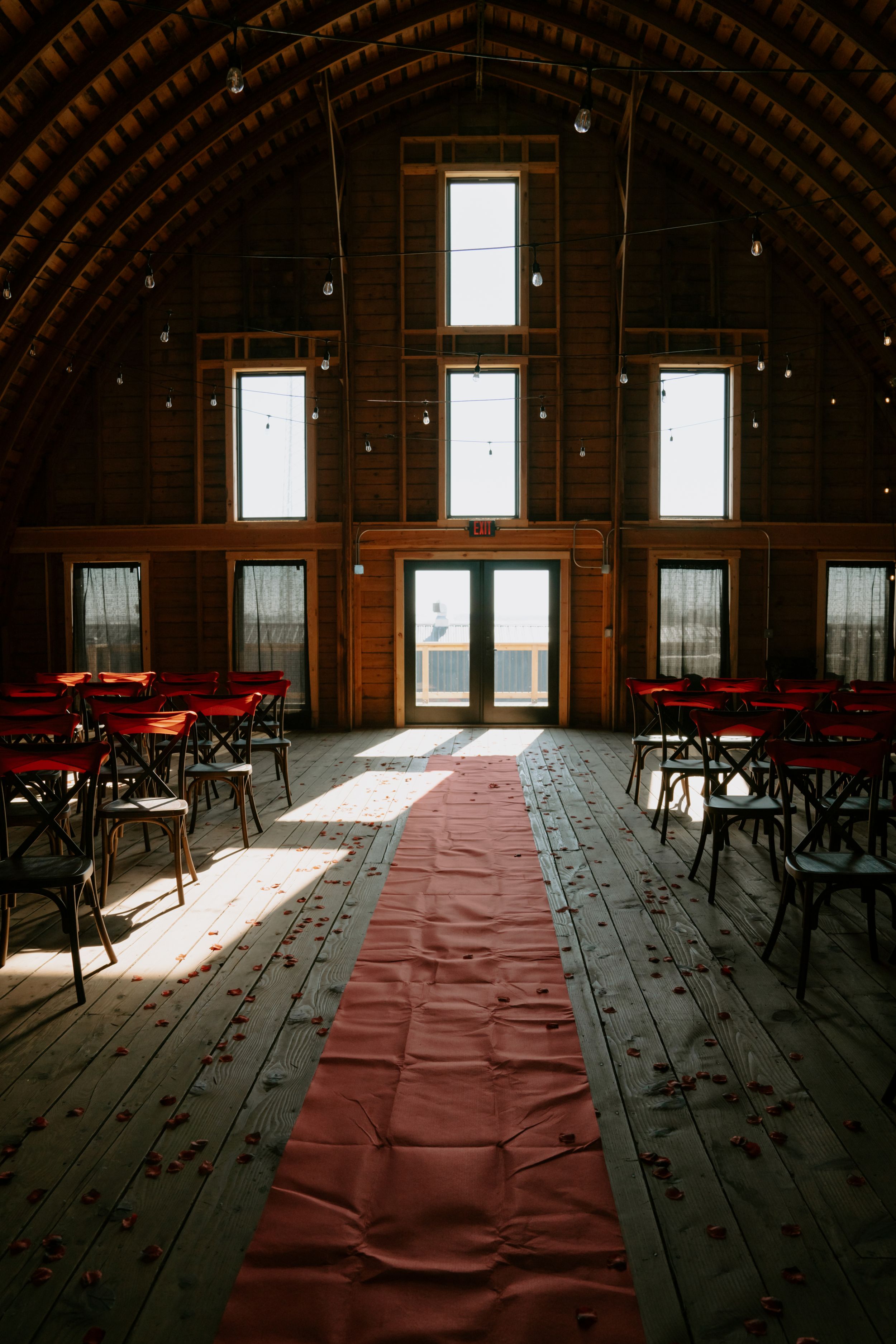A rustic barn venue interior with red carpet aisle and natural light streaming through windows.