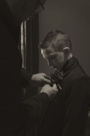 Intimate wedding preparation moment captured in dramatic low-key lighting.