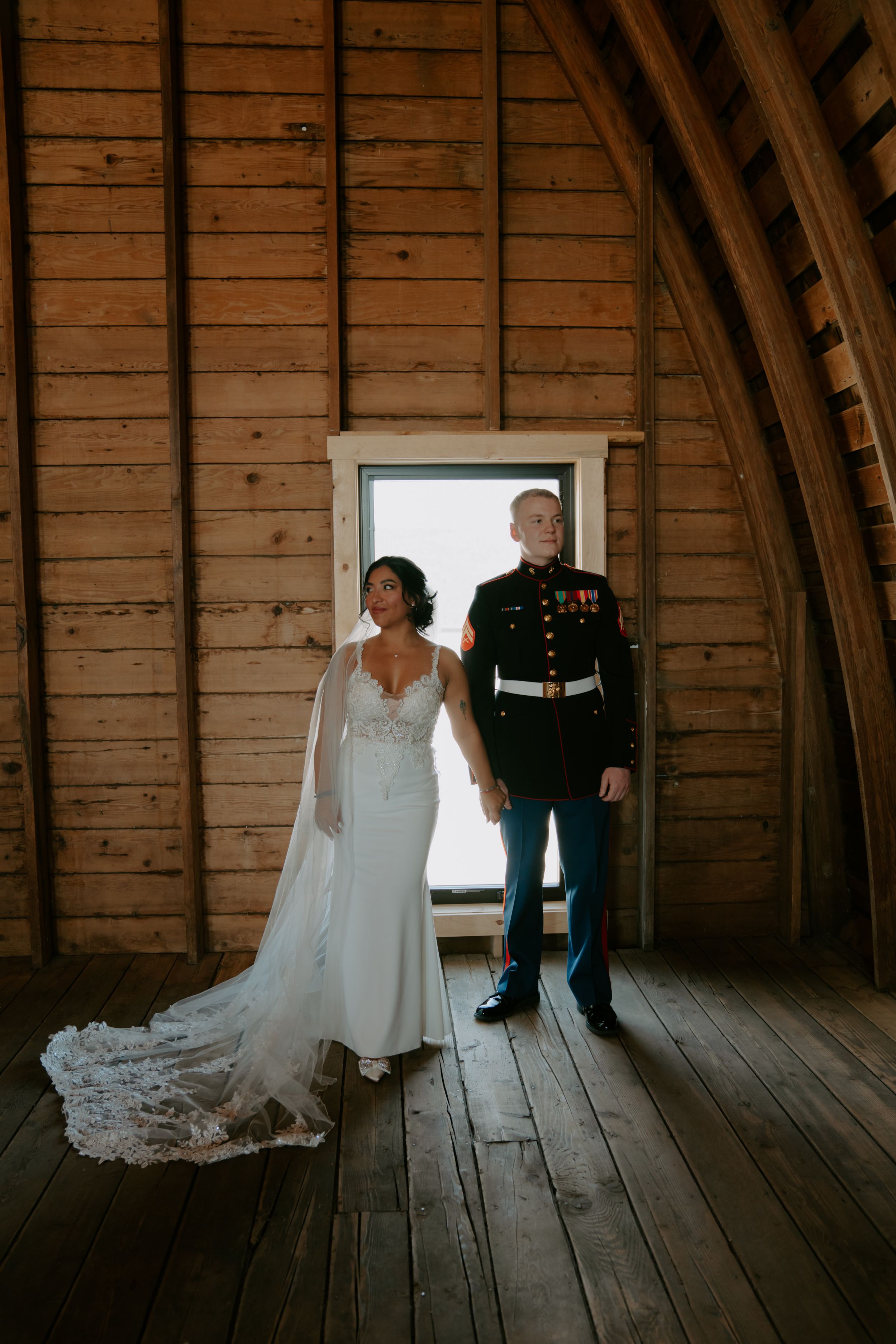 A wedding couple in an atmospheric rustic barn with wooden walls and natural light streaming through a window.