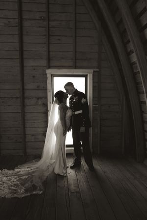 Silhouettes of a wedding couple in a rustic wooden barn with dramatic lighting from a window.