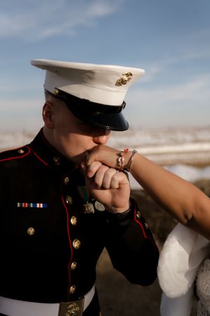 Close-up shot of a Marine in dress uniform kissing a hand against a blue sky background.