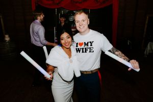 Wedding reception guests dance and celebrate on a dark dance floor with festive lighting.