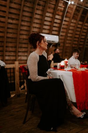 A guest in an elegant black and white dress sits at a decorated reception table with red accents.
