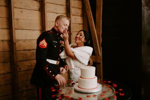 A couple shares a playful moment while cutting their wedding cake in a rustic barn setting.