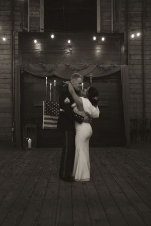 A romantic first dance in front of an American flag in a dimly lit rustic venue.