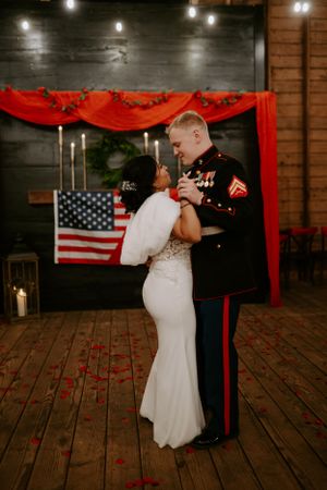 A couple shares their first dance in front of American flag decor and red drapery.