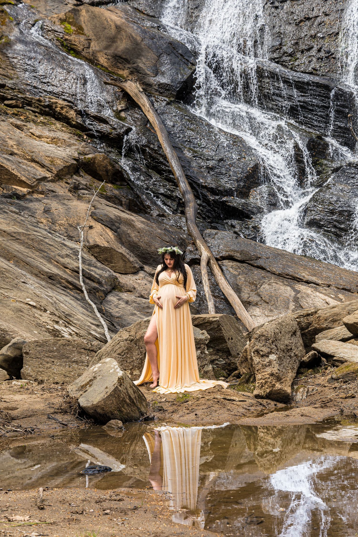 A peachy-colored gown reflects in the pool of water beneath a cascading waterfall over rocky terrain.