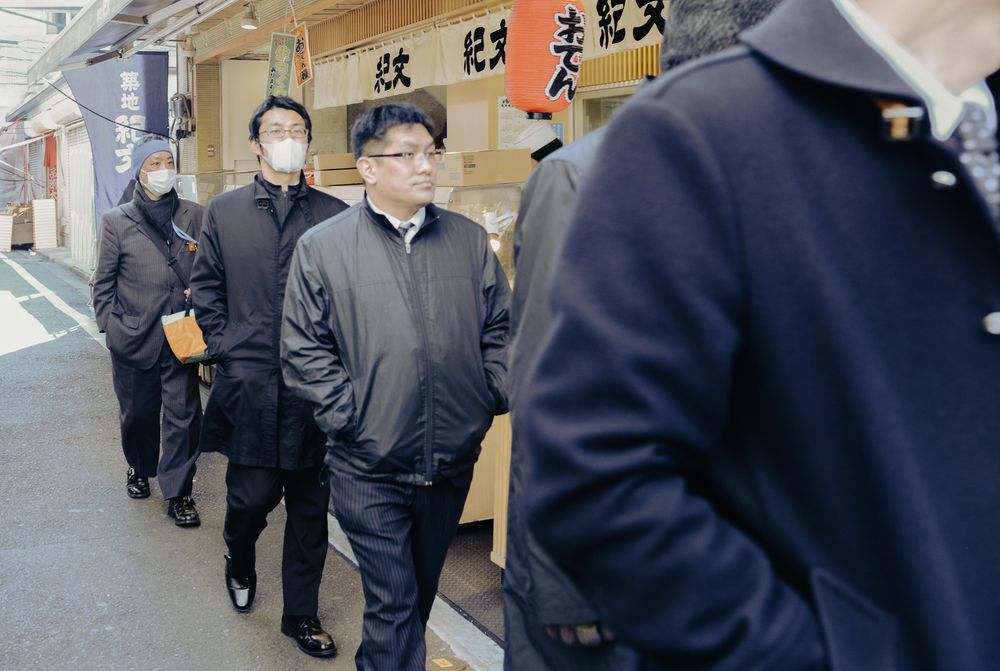 Commuters walking through a crowded subway station corridor in business attire.