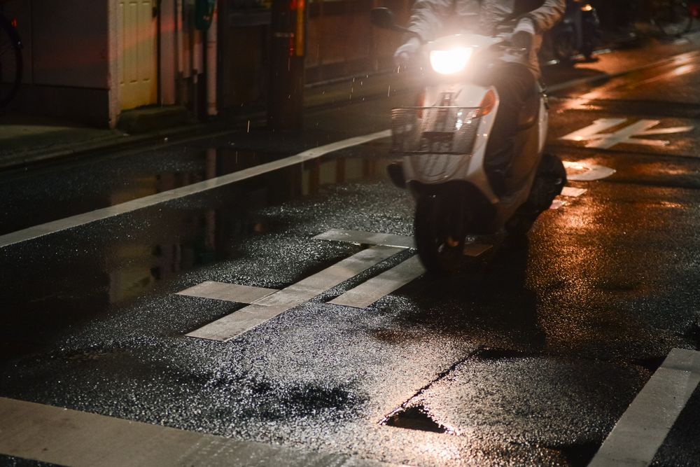 Wet city street at night with car headlights reflecting off the rainy pavement.
