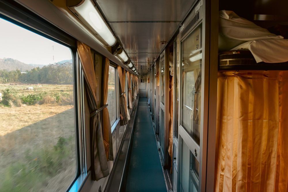 Sunlit view through a train window showing rural landscape and interior corridor.