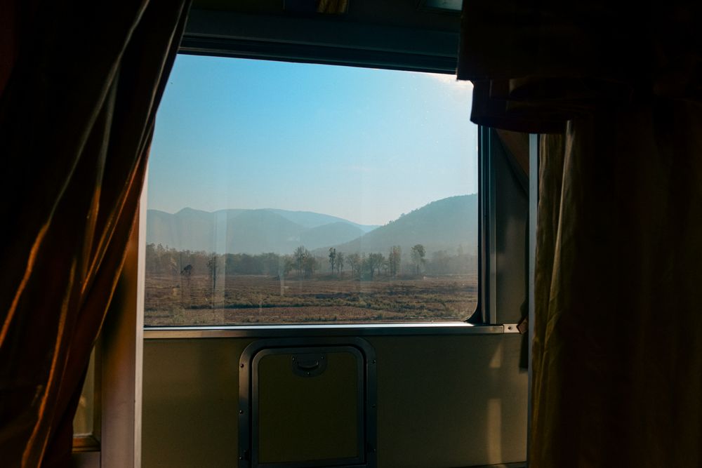Beautiful sunset view through a train window with mountains visible in the distance.