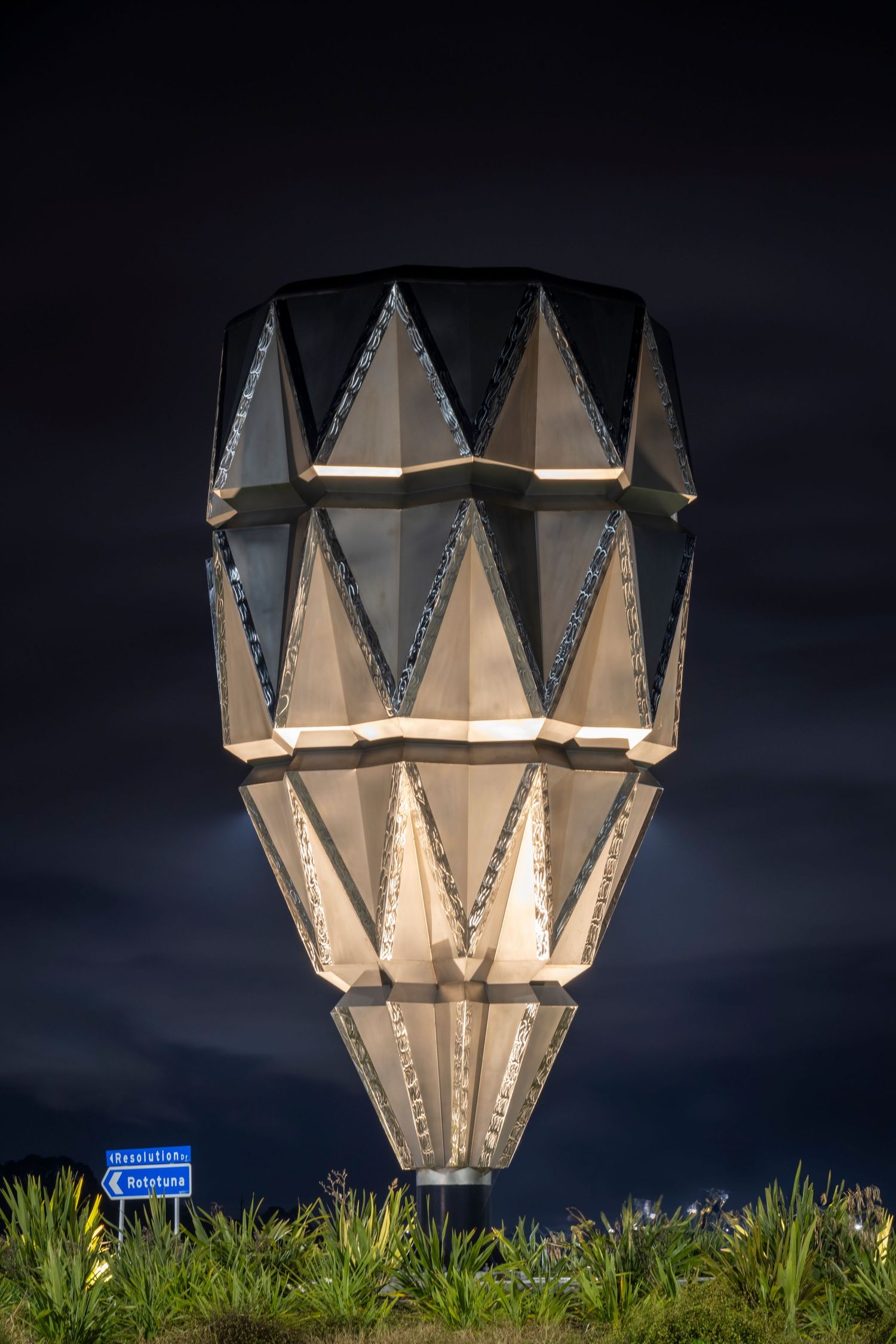 Futuristic, faceted structure lit from within, shaped like a cone or lantern, set against a dark night sky.