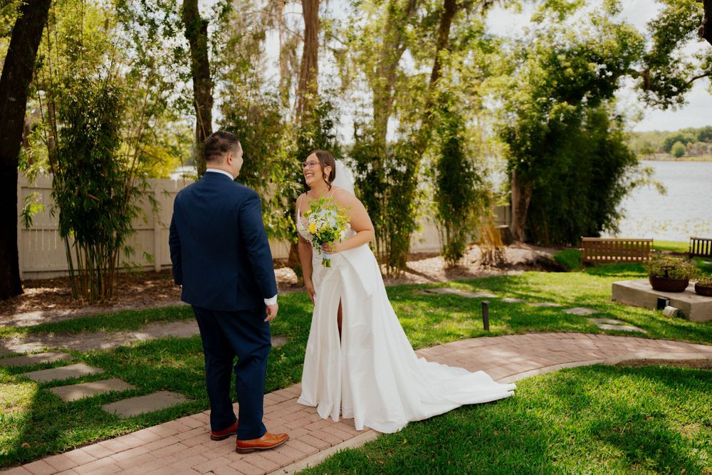 Two people share a special moment in a lush garden setting with a stone pathway and green lawn on a sunny day at enzos on the lake.