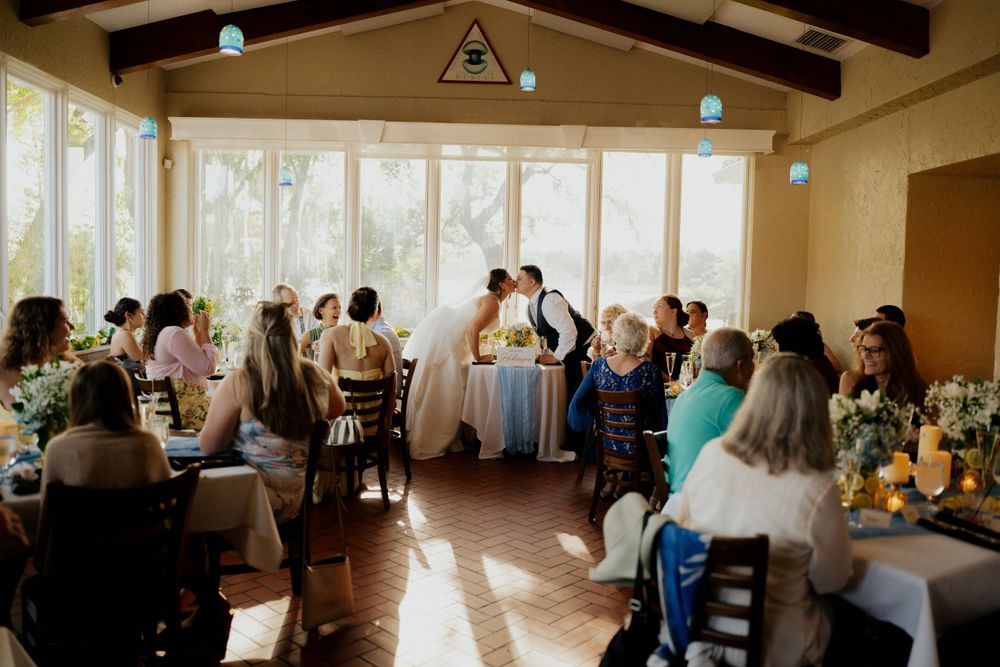 Guests watch a celebration in a sunlit reception venue with exposed wooden beams and elegant table settings.