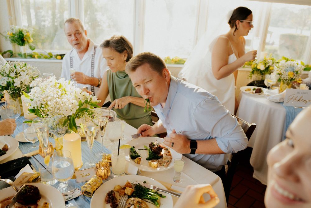 Wedding guests laughing and enjoying dinner at a reception table decorated with white floral centerpieces.