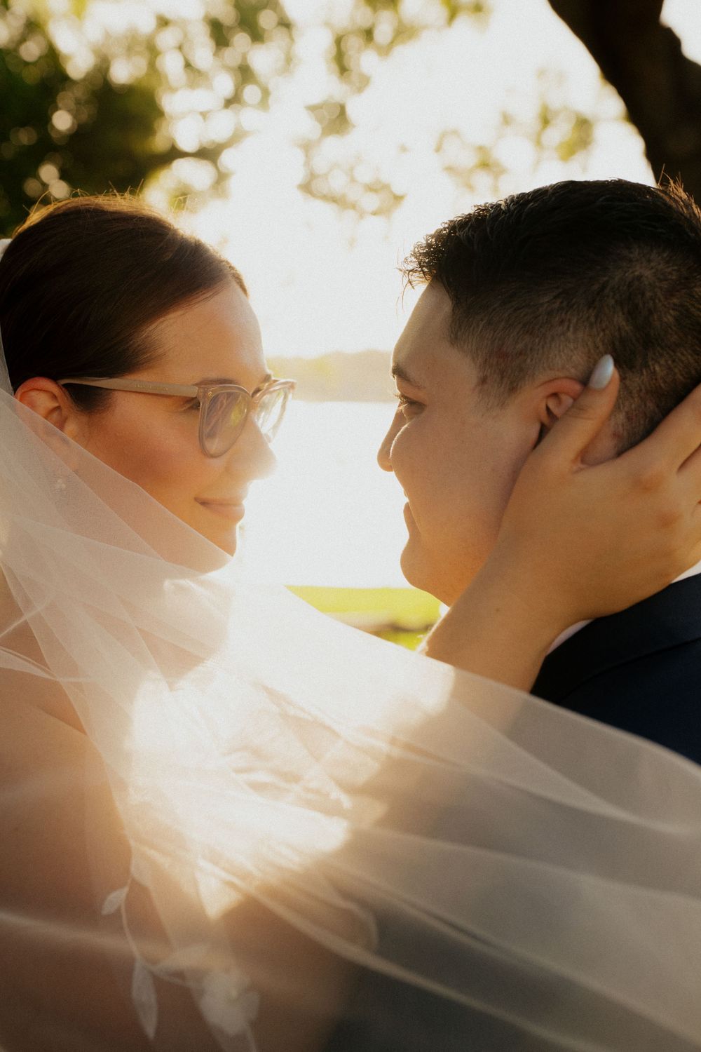 Romantic close-up of a couple with flowing veil caught in golden sunlight.