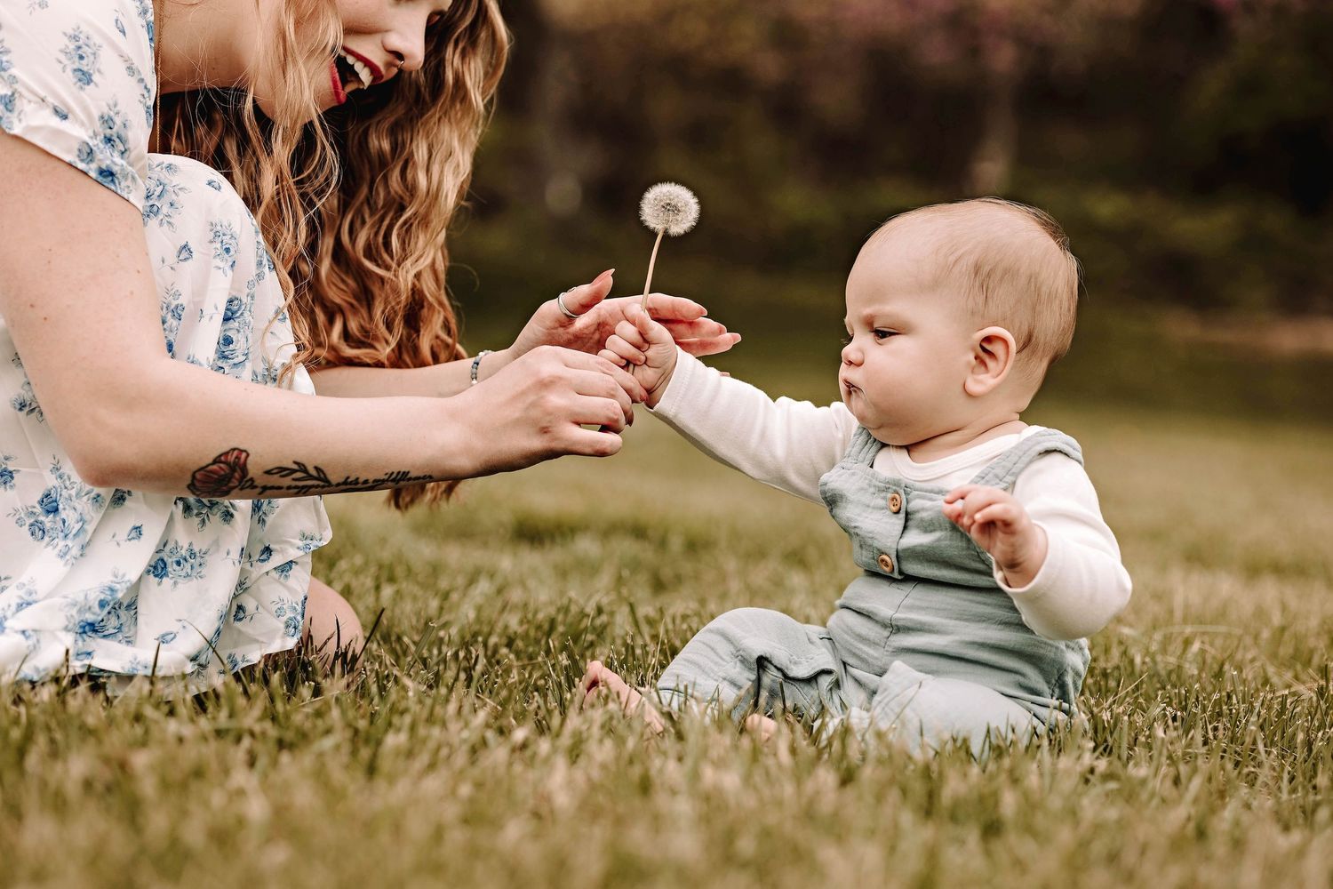 A mother holds a dandelion flower while sitting with a baby on grassy ground during a sunny day outdoors with her family near Bel Air MD