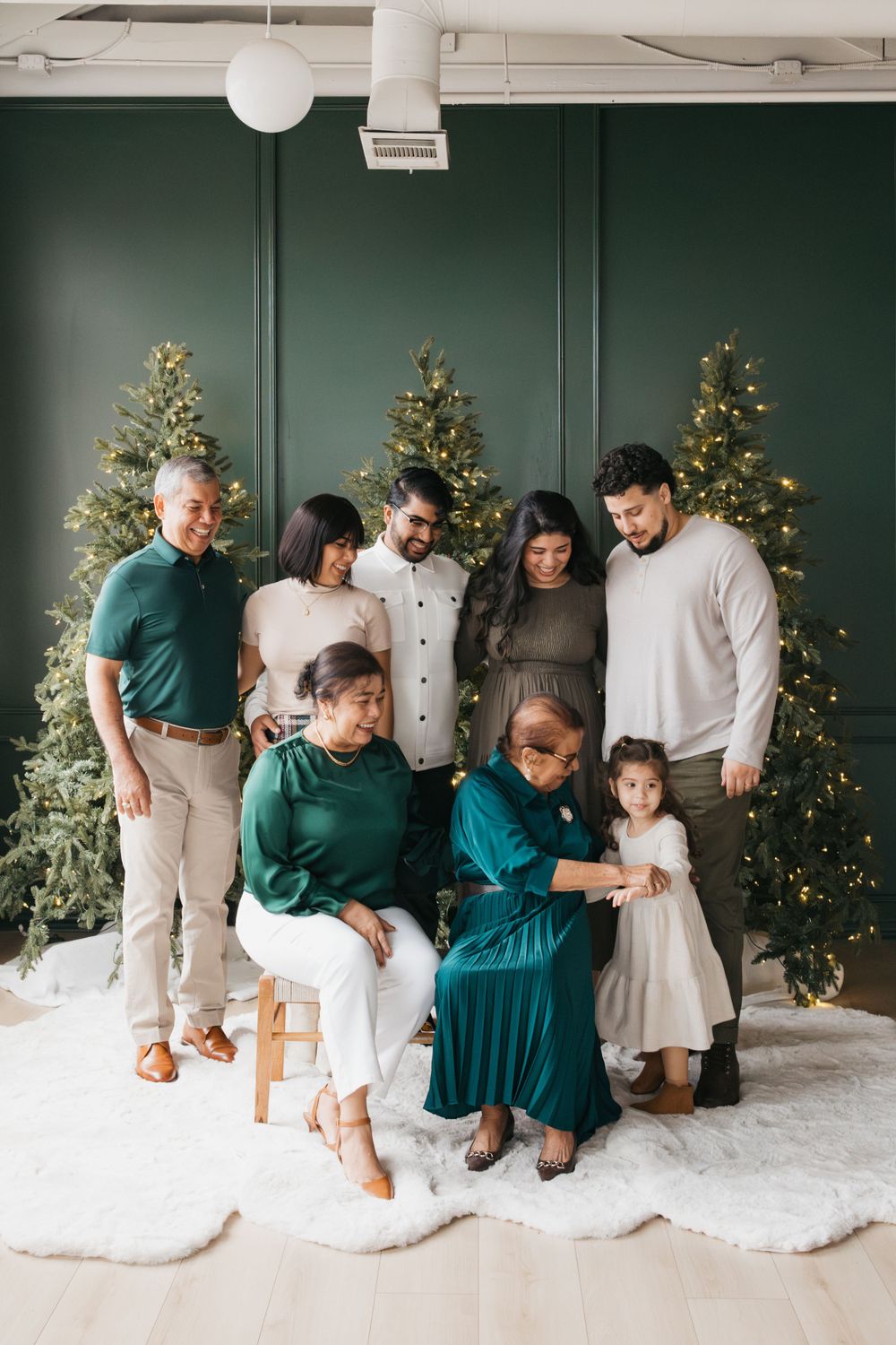 A multigenerational family group poses together for a holiday photo in front of illuminated Christmas trees.