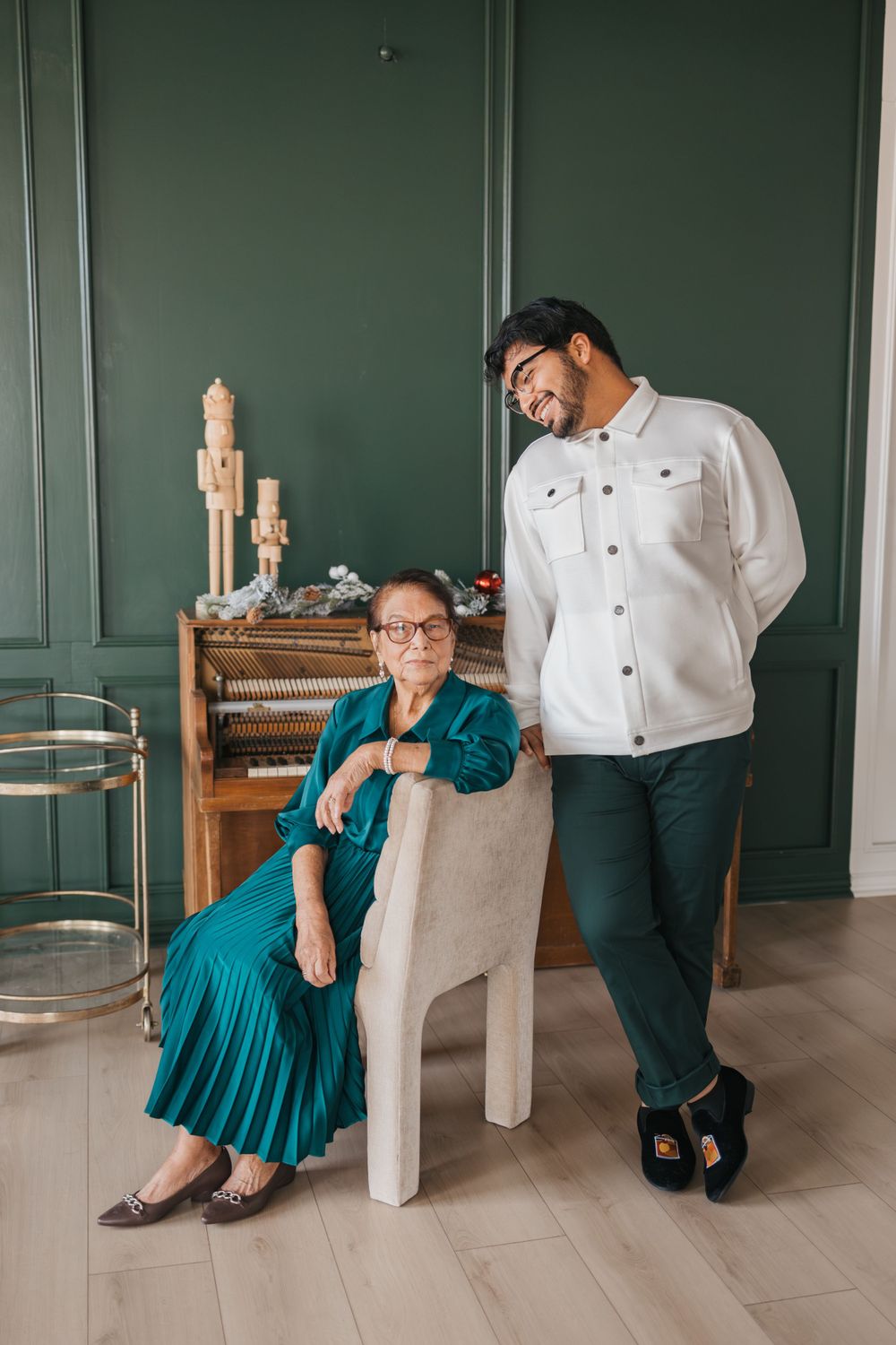 Two people pose elegantly in front of a green wall with candles and home decor.