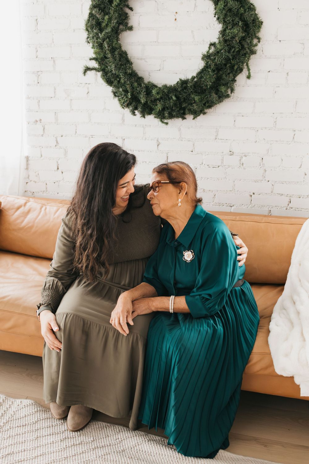 Two people sharing an intimate moment on a tan leather couch beneath a green wreath.