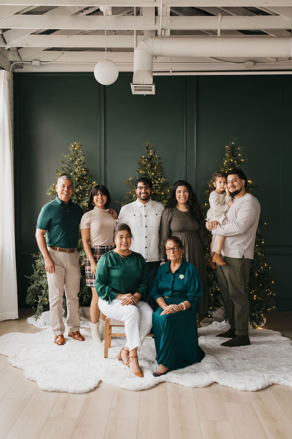 Holiday family portrait with matching outfits in green tones against decorated Christmas trees.