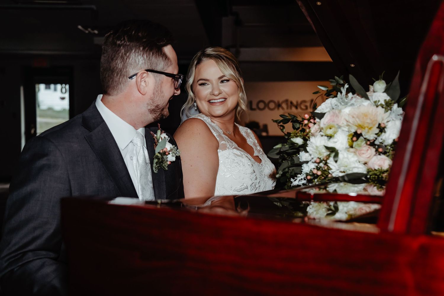 A couple sits together in a classic red car at their wedding celebration with white floral bouquet decorations.