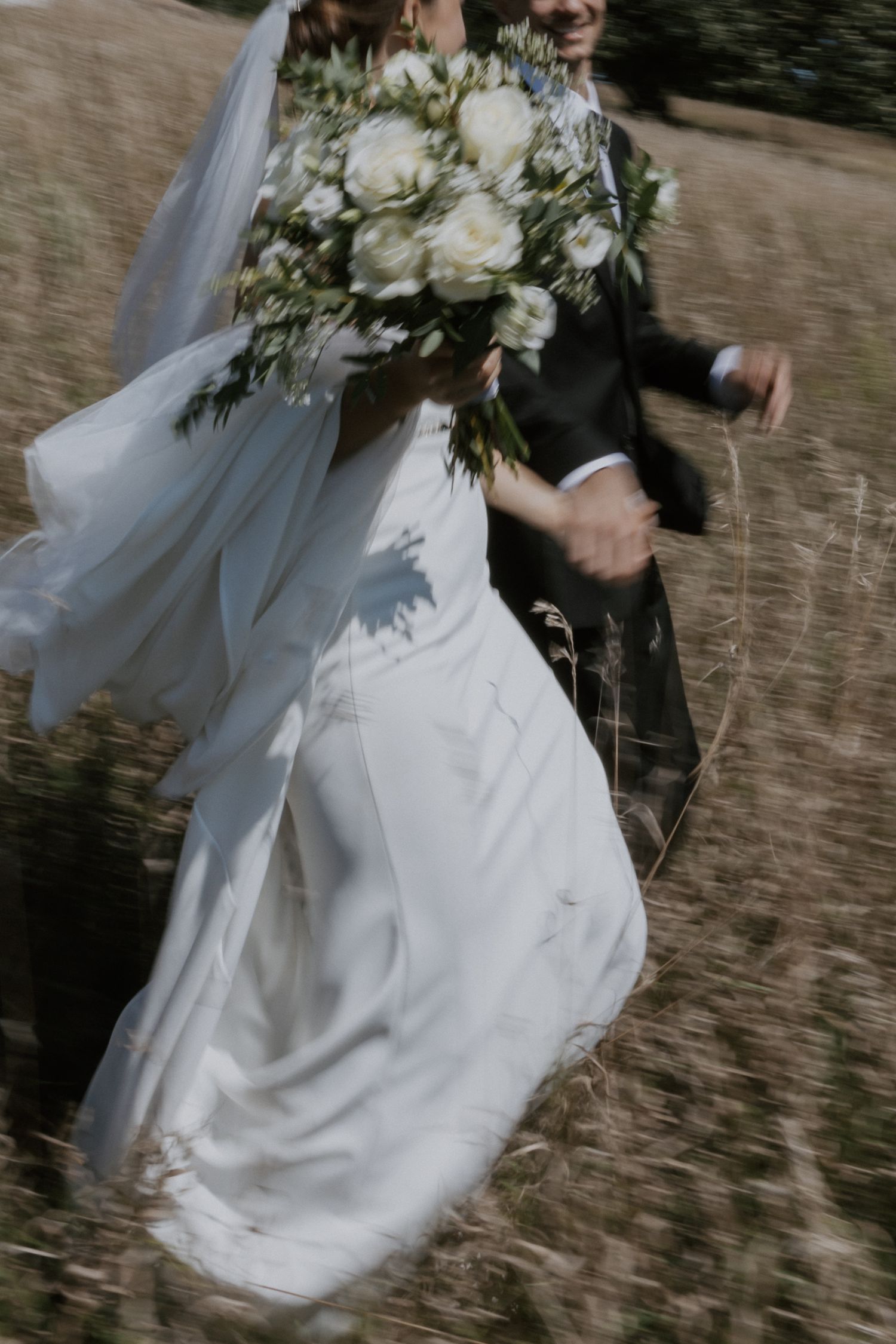 A flowing white wedding dress and bouquet of white roses captured in motion during an outdoor ceremony.