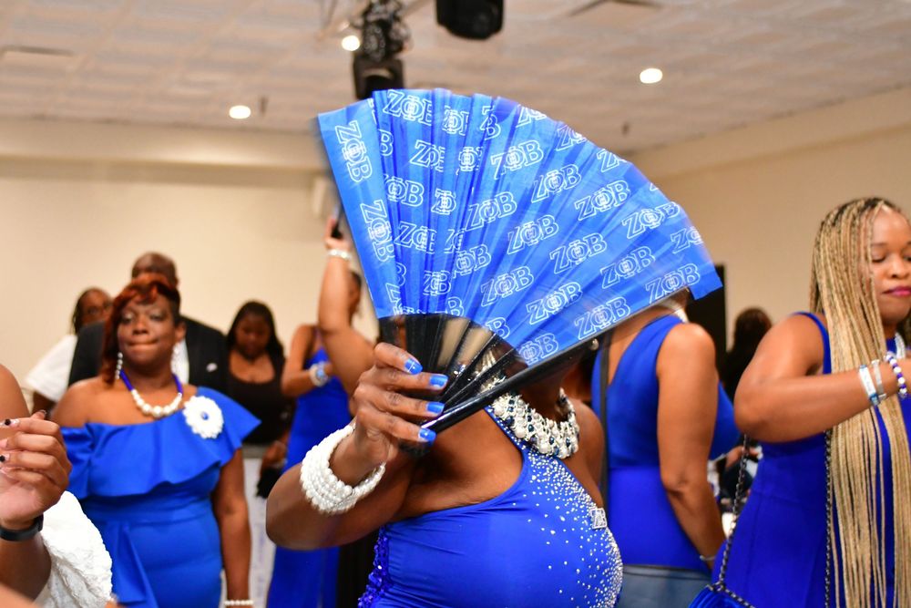 People dance at a celebration holding bright blue handheld fans while wearing coordinated royal blue attire.