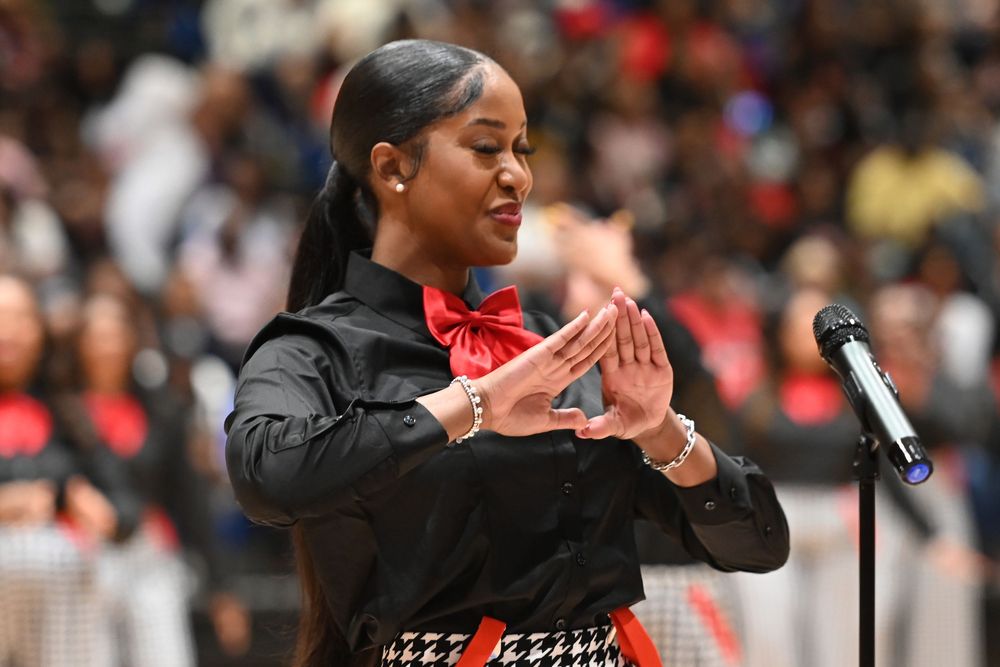 A music conductor in a black outfit with red bowtie gestures with their hands during a performance.