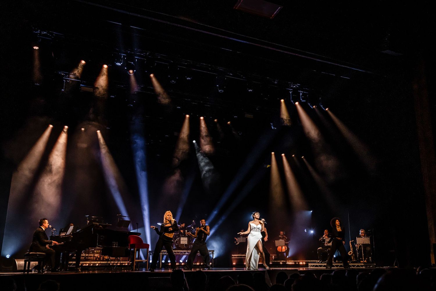 Concert performance with orchestra and performers under dramatic blue and white spotlighting.