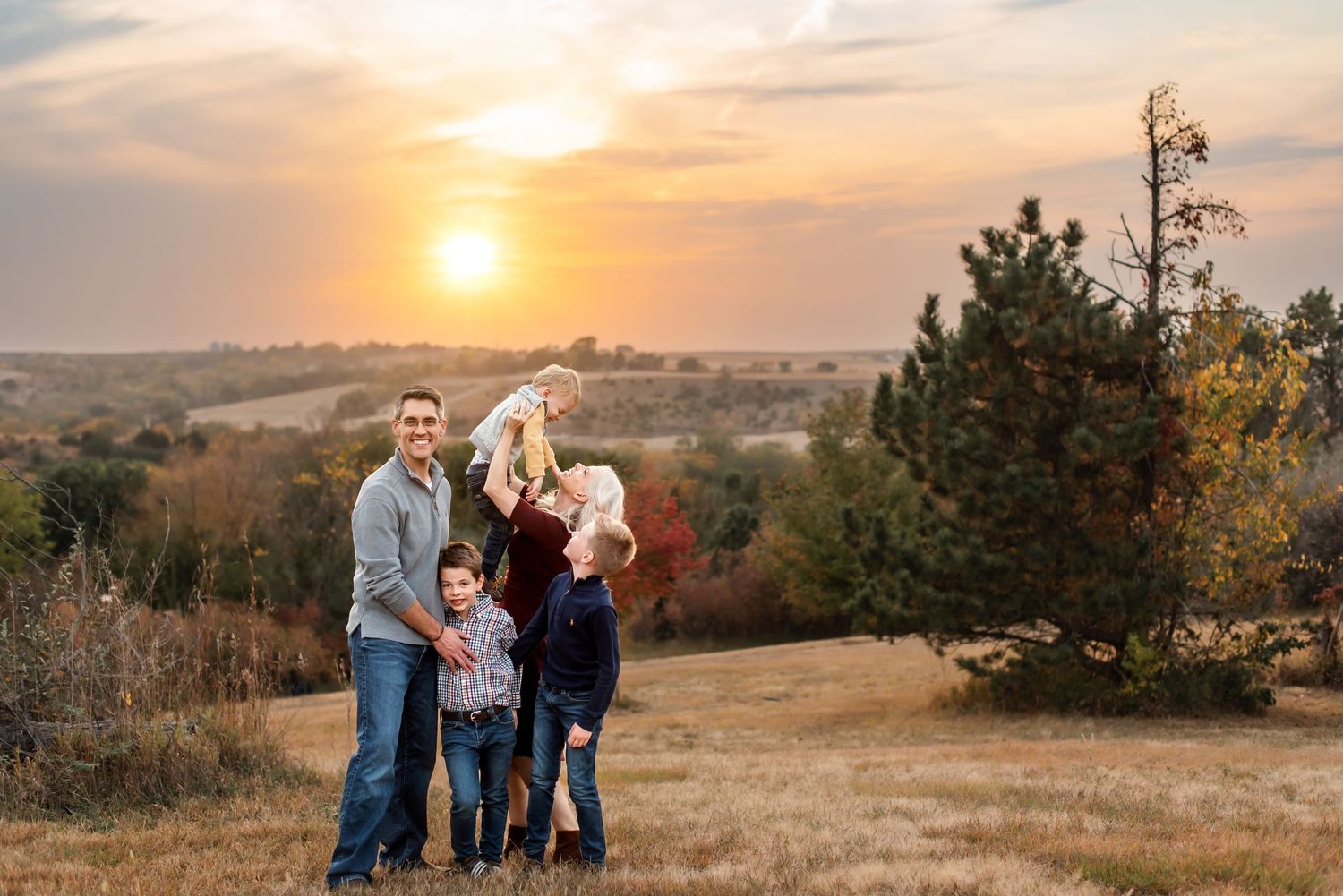 A group stands together on a hilltop during golden hour sunset with rolling autumn hills in the background.