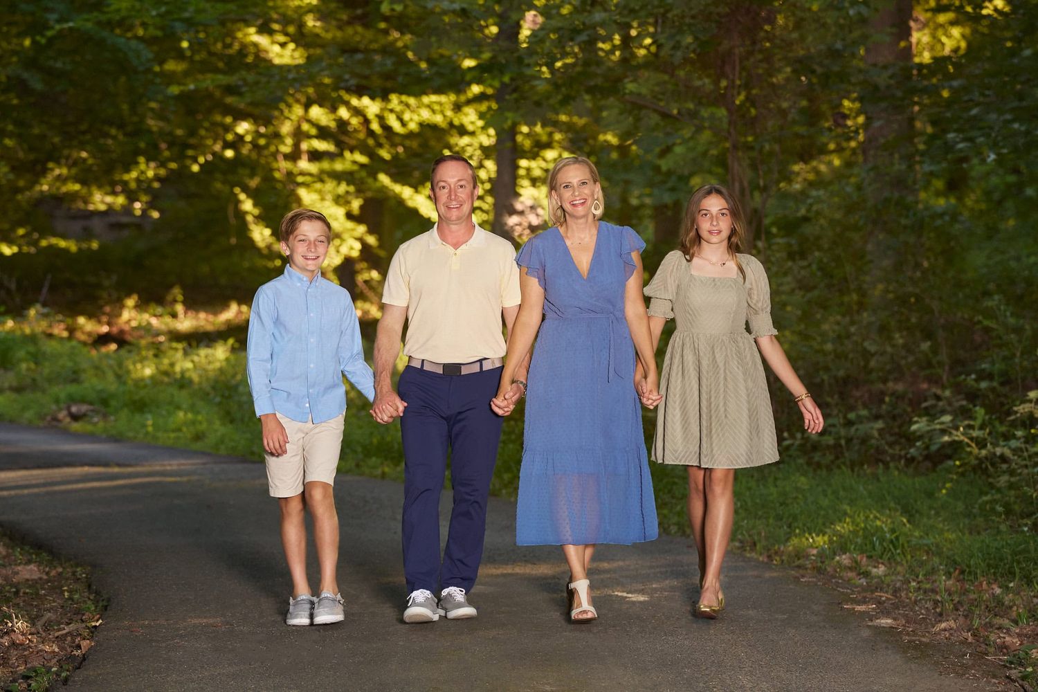 Parents and boy and girl tween holding hands walking on a wooded driveway path