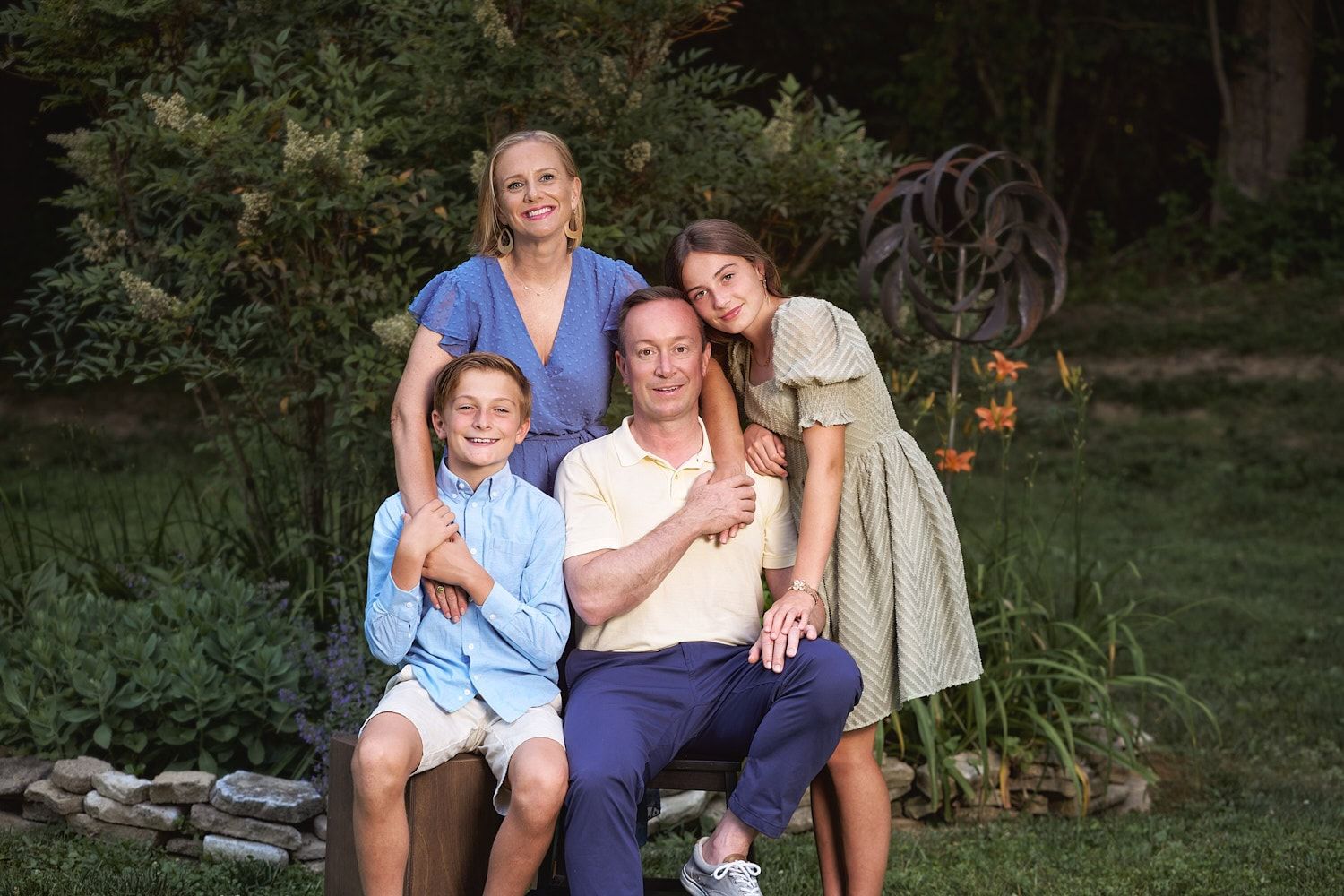 Parents and boy and girl tween with family dog sitting  in front of circular planting