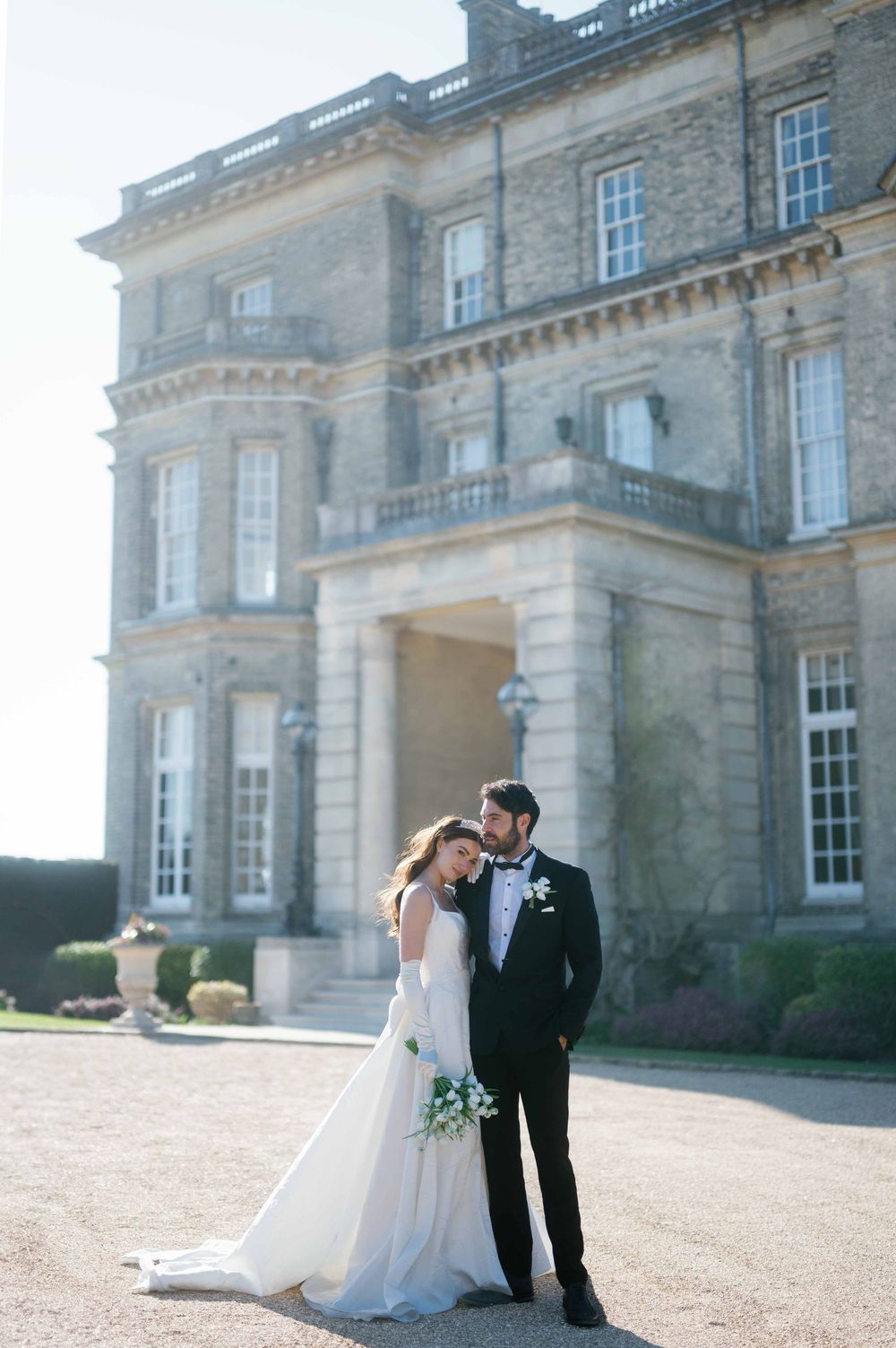A couple shares a romantic moment outside a grand historic mansion with elegant stone architecture and tall windows.