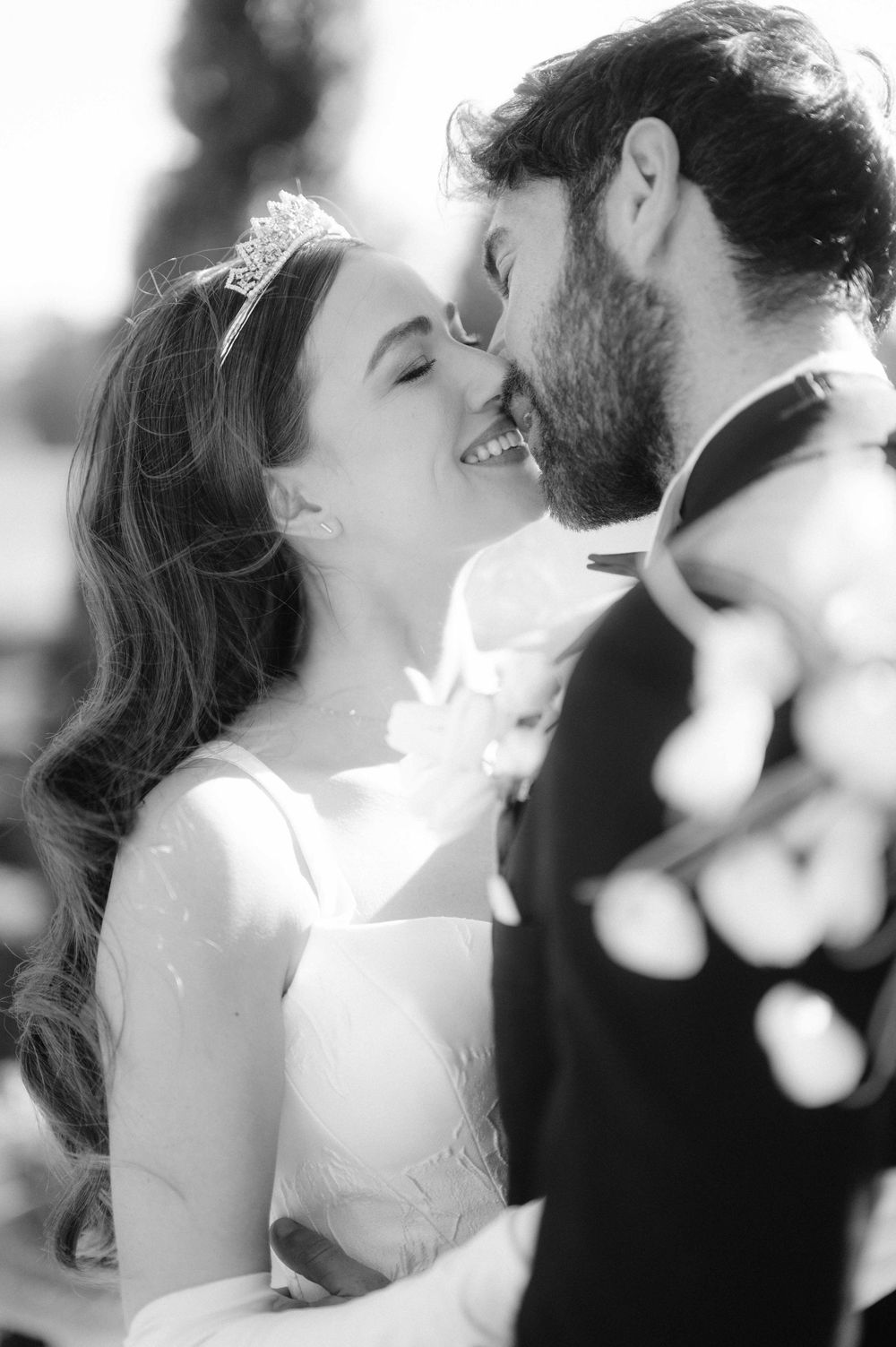 A romantic black and white wedding photo showing a tender moment between a bride in white and groom in a suit.