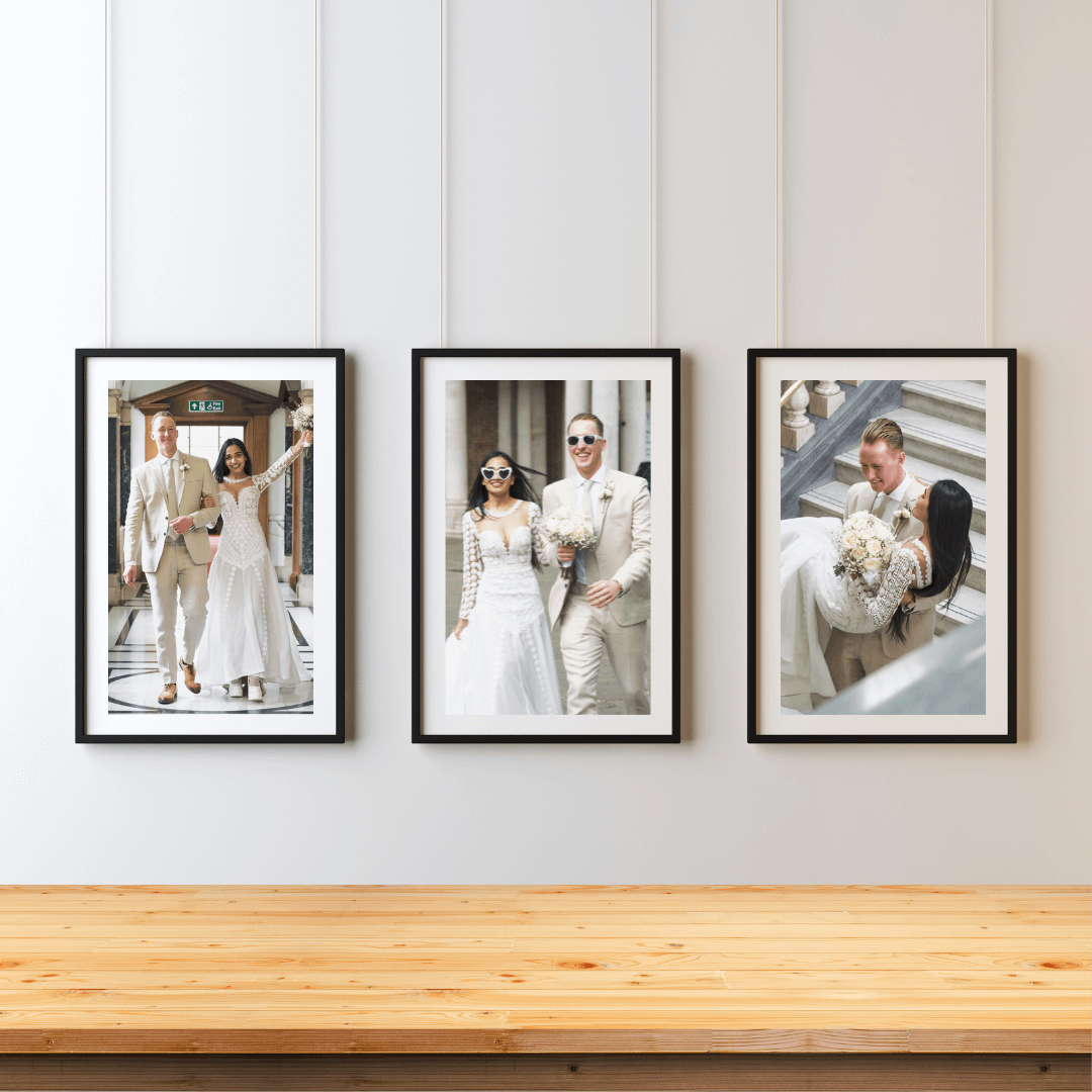 Three framed wedding portraits displayed on a white wall above a wooden surface.