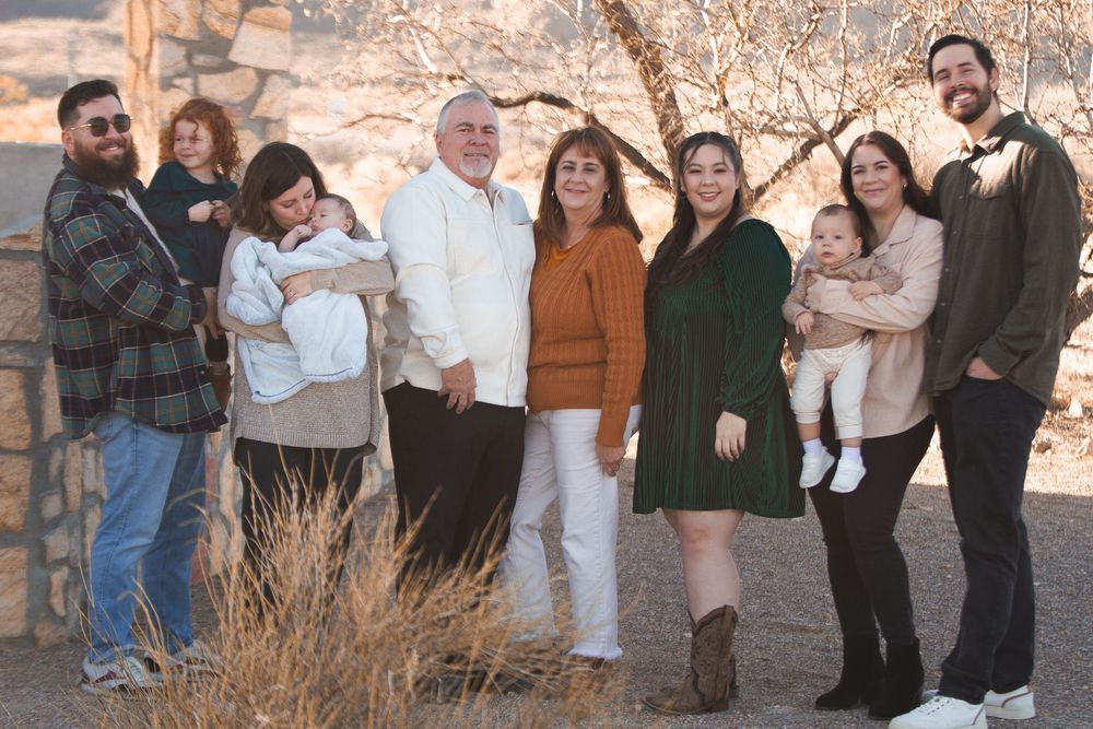 Large family group portrait outdoors in desert setting, smiling adults holding babies, dressed in coordinated fall outfits.