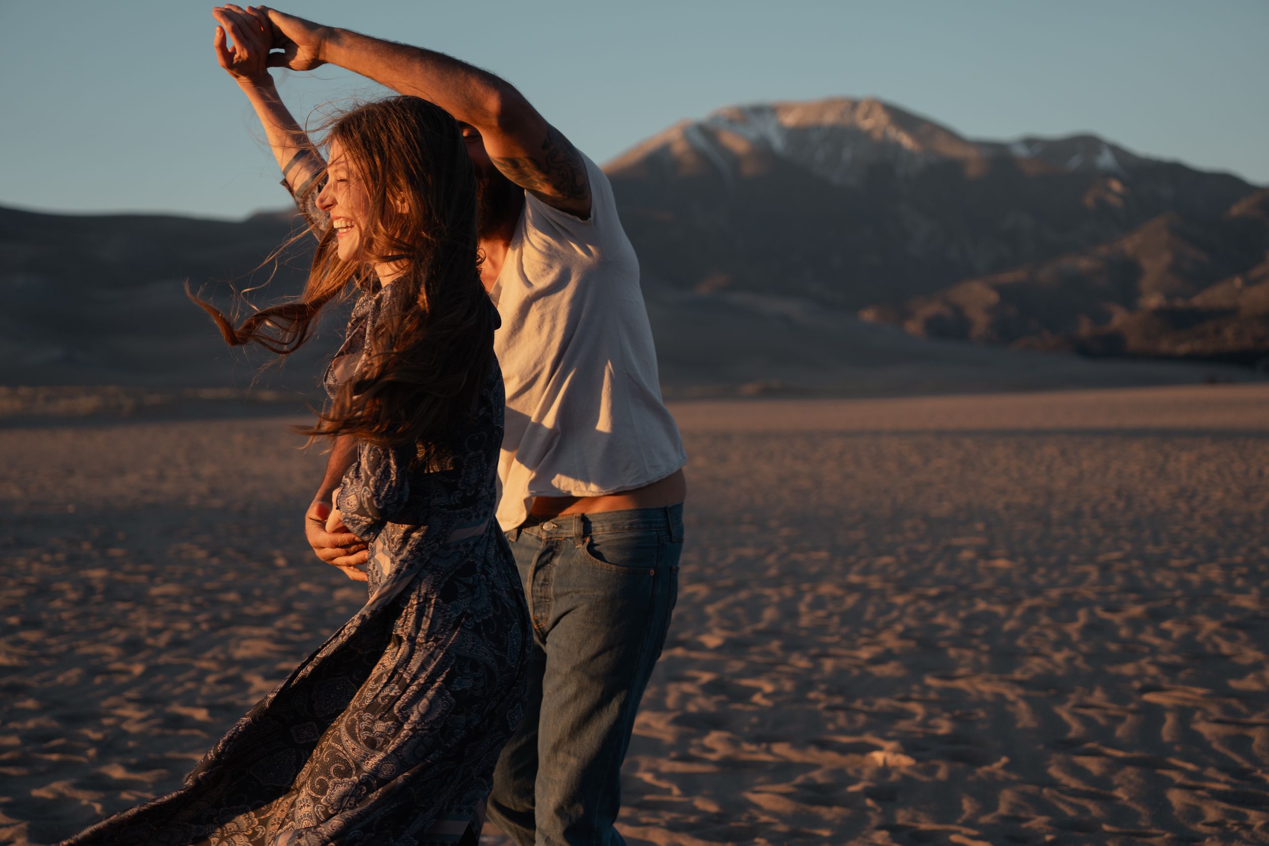 A couple dances together on a beach at sunset with mountains in the background. Great sand dunes elopement adventure