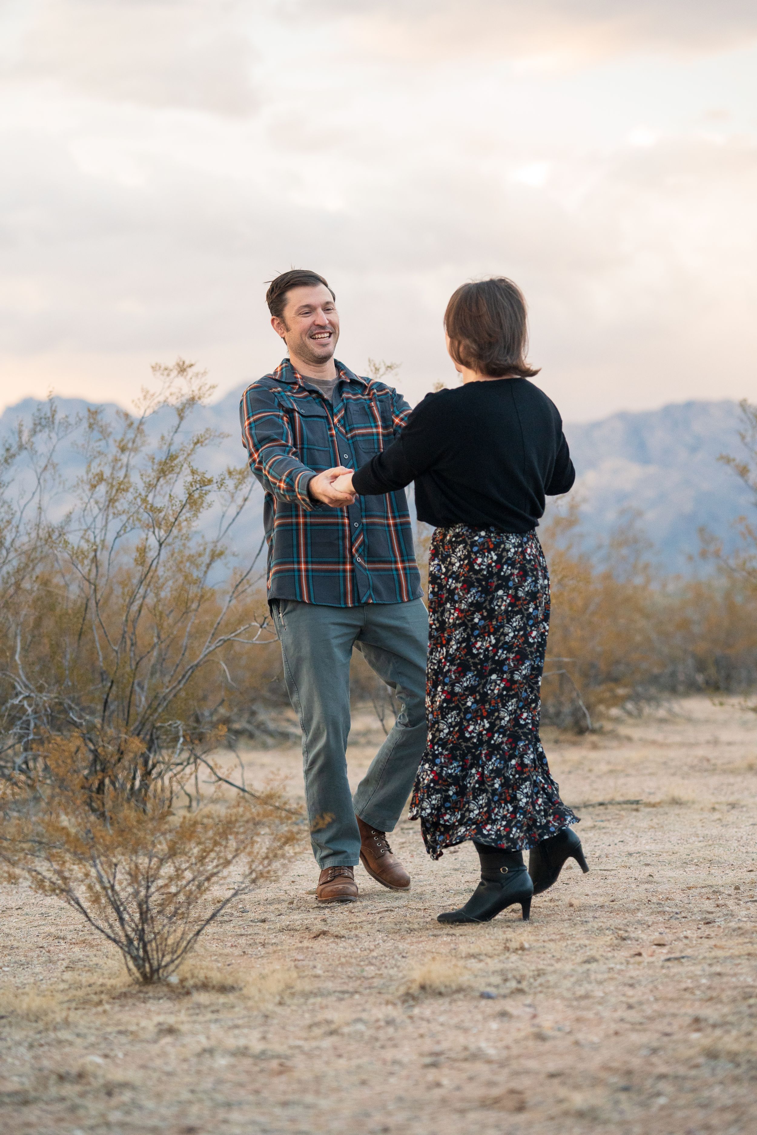 A couple dances together in the desert at sunset with mountains in the background. arizona adventure photos. engagement photograph