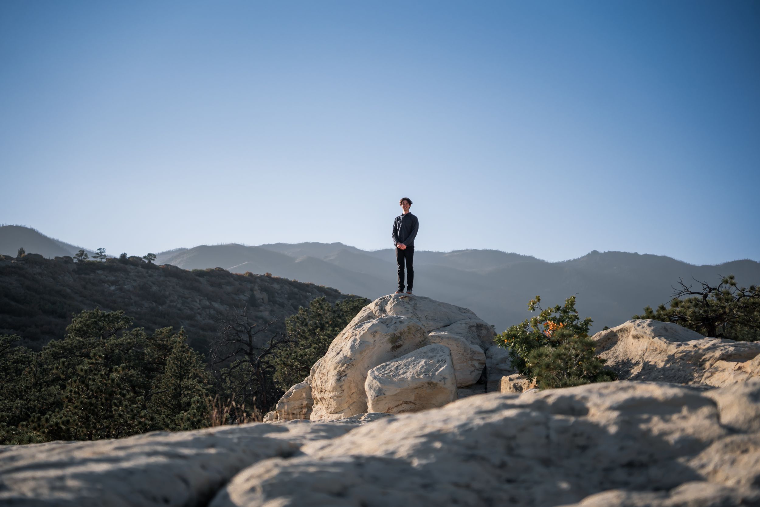 A silhouetted person stands on a large rock overlooking mountain vistas.
