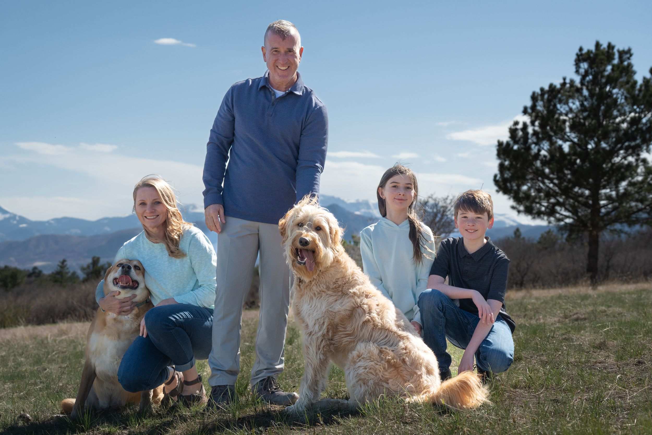 A family and their two dogs pose for a portrait on a grassy hill with mountain views. family session outdoor