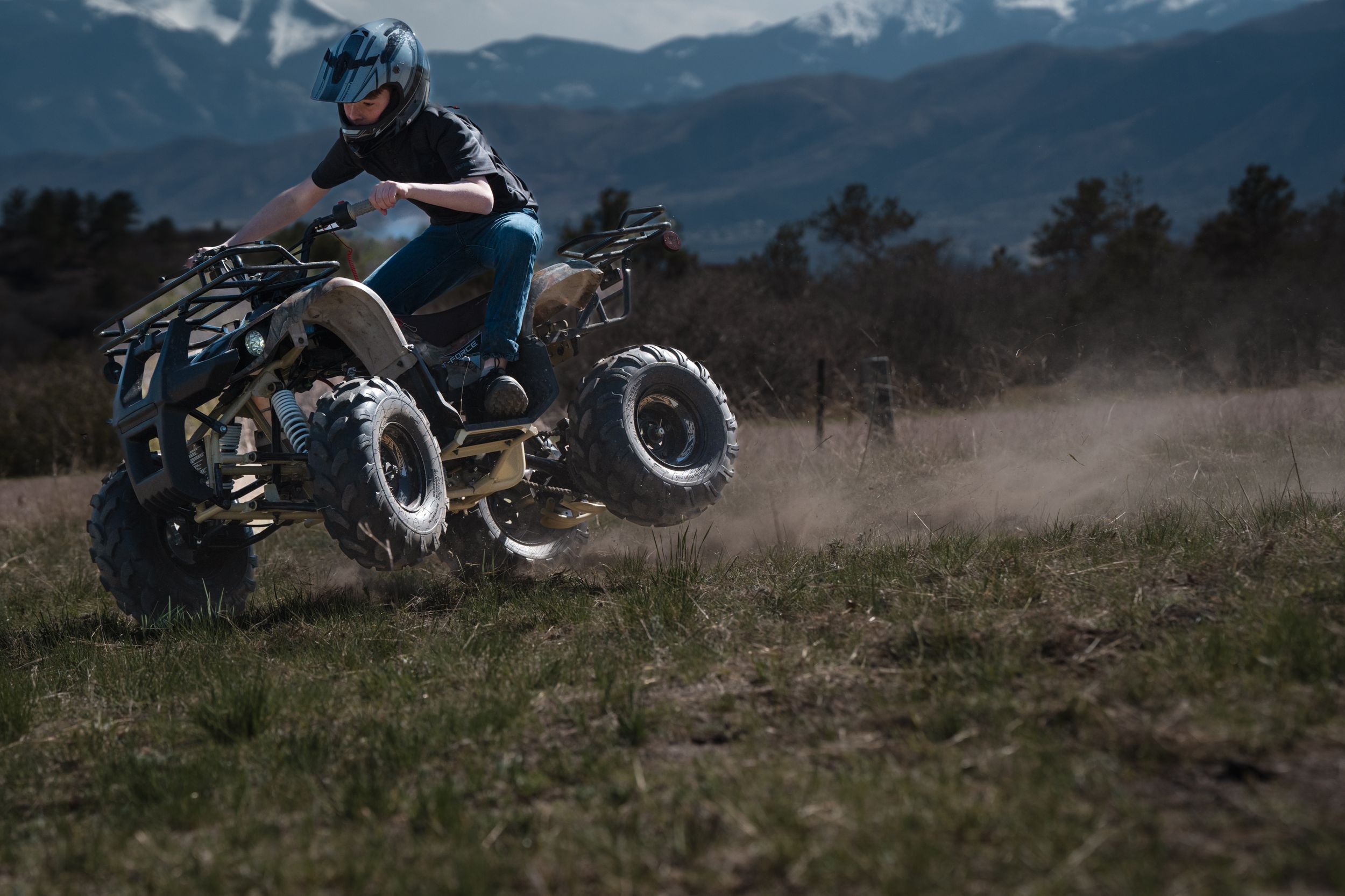 Someone rides an ATV through a dusty field with mountains visible in the distance.