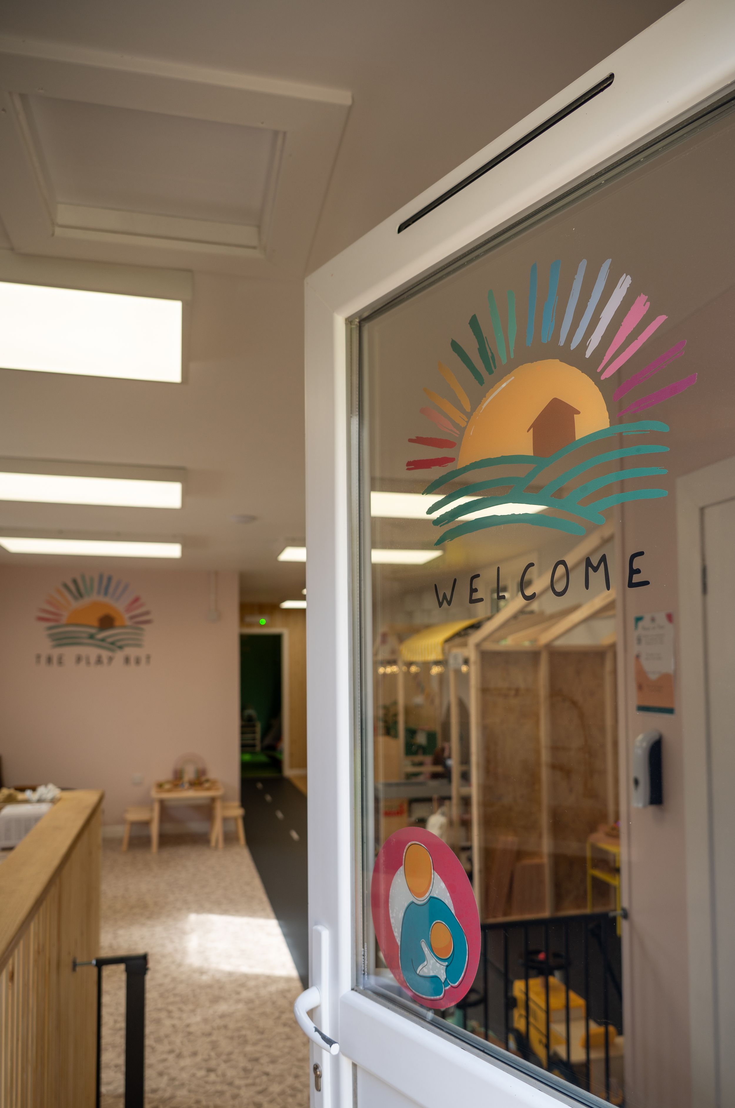 A decorative welcome sign on a glass door features a colorful sunset logo with palm fronds and tropical design elements.