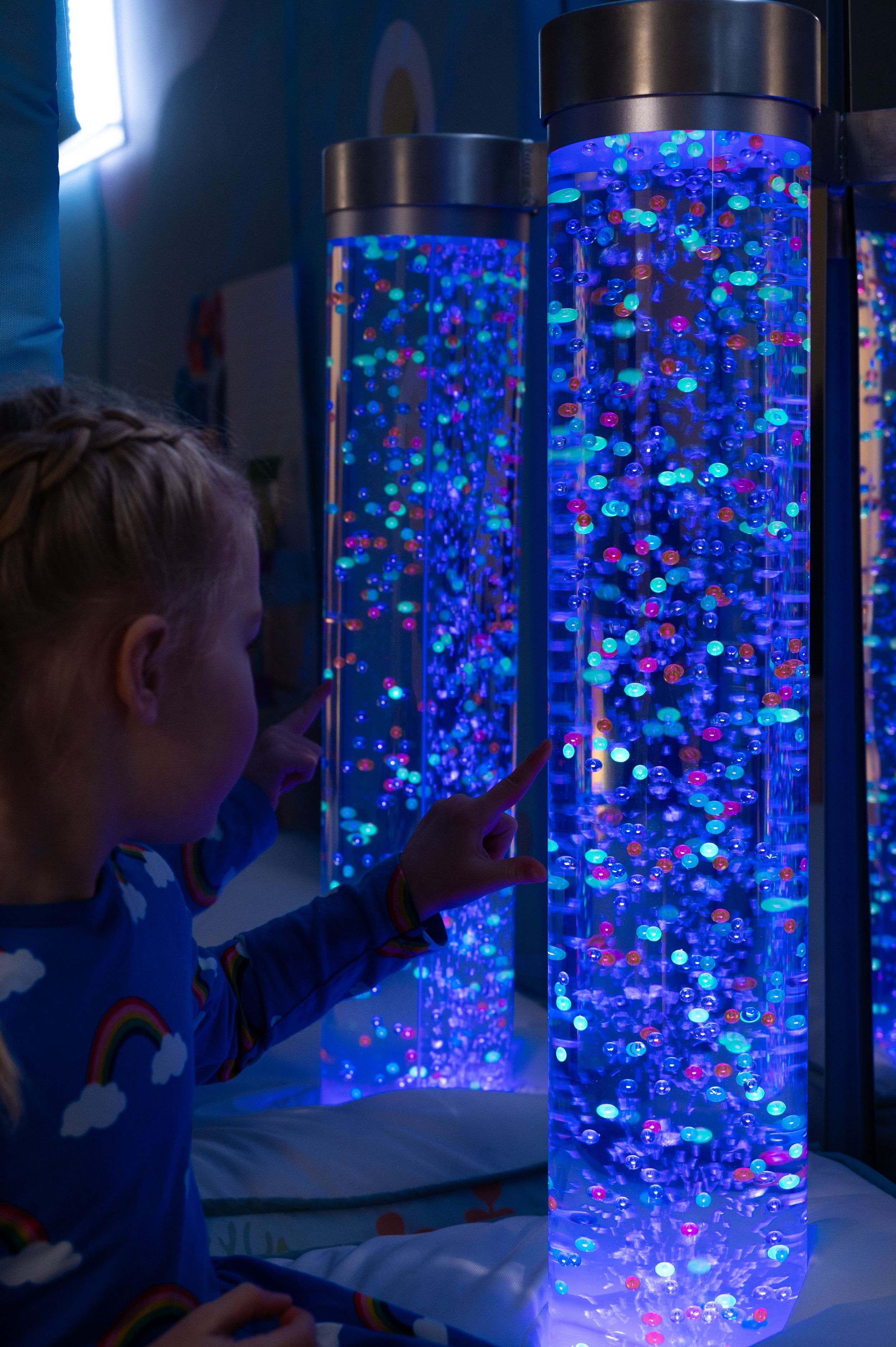 A glowing blue sensory bubble tube creates a mesmerizing display of illuminated bubbles in a dark room.