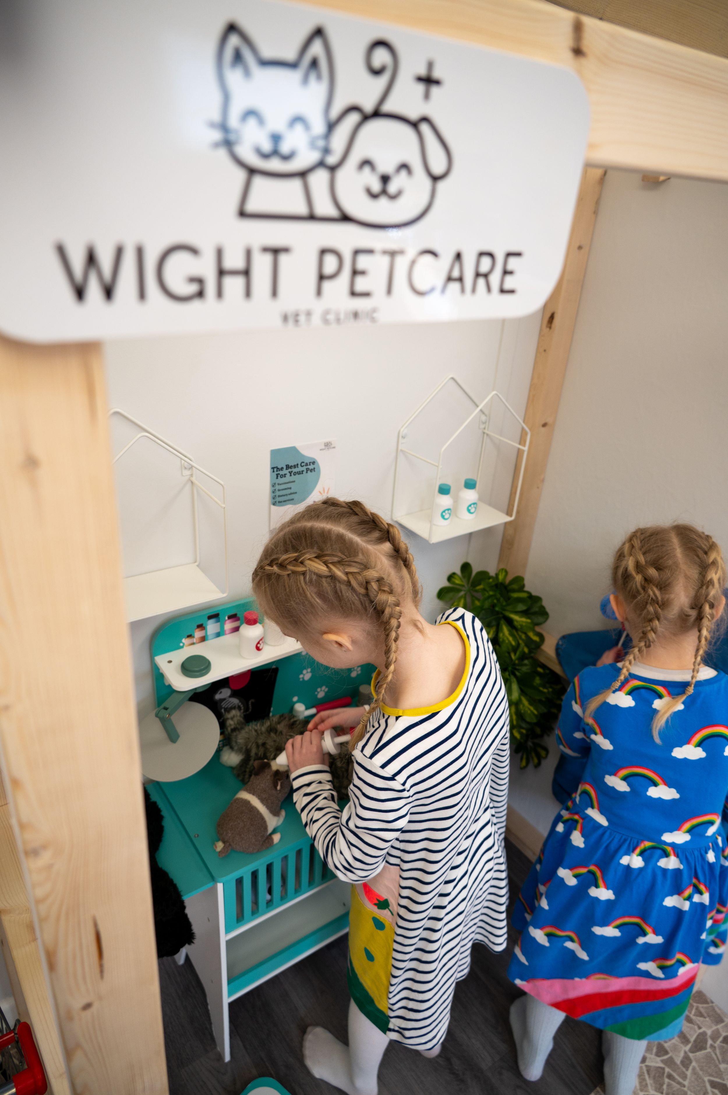 Children play with toy veterinary equipment at Wight Petcare play area featuring a cat and dog logo on the wall.
