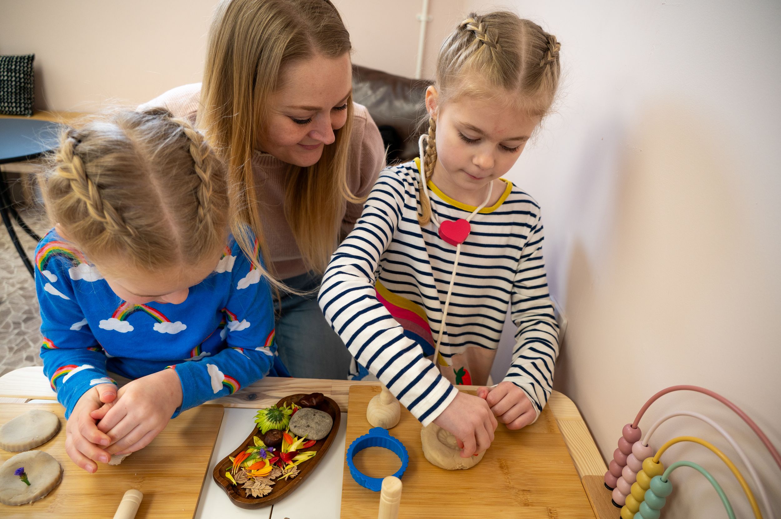 Children and caregiver sit at a wooden table doing activities with educational toys and wooden rainbow arch.